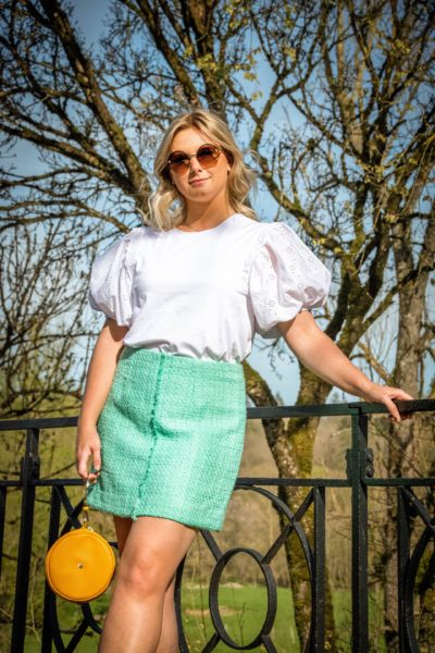 A blonde woman wearing a handmade skirt made in Belgium, made on the size of the client and a white lace top from Zara with puffy sleeves.